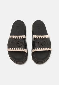 Sorte slidesandaler med en tykk rem som har preget merkevare og beige fletteakenter. Mykt gummimateriale med teksturert såle.