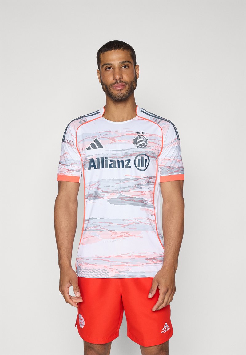 Jersey bianco a maniche corte con motivi astratti rosa e grigi, dettagli rossi e branding nero; abbinato a pantaloni corti rossi con un logo.