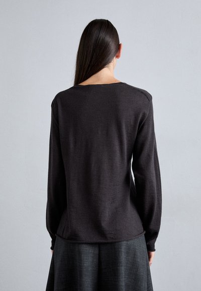 Dark gray long-sleeve top with a round neckline, smooth texture, and relaxed fit. Cutout shoulder details, paired with a dark skirt.