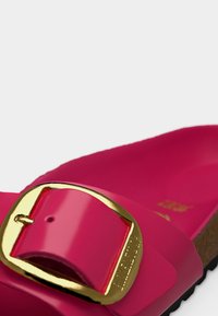 Ροζ σανδάλι με γυαλιστερή επιφάνεια, με μεγάλο χρυσό τοκά και υφή στην επιφάνεια του πατουσίου, σχεδιασμένο για άνετη εφαρμογή.