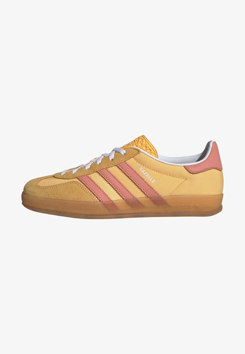 O sneaker amarelo de camurça e couro possui três riscas cor-de-rosa, atacadores brancos, sola de borracha e calcanhar texturizado. A marcação na lateral diz "Gazelle."