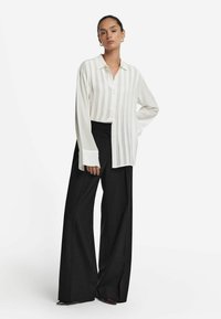 Vit långärmad skjorta med knappar och vertikala ränder, matchad med höga svarta vida byxor med en slät textur och avslappnad passform.