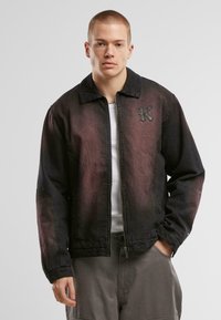 Svart og burgunder gradient denimjakke med glidelås foran, krage og teksturert brodert bokstav "K" på venstre bryst.