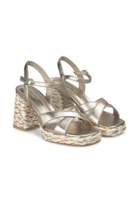 Sandali strappy in oro metallico con tacco a blocco in stile espadrilles intrecciato. Presentano cinturini incrociati e chiusura con fibbia. Suola piatta.