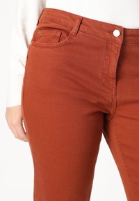 Jeans v rustovej farbe so strihom straight fit, obsahujúce predné vrecko, zips a dizajn s piatimi vreckami. Textúrovaná denimo tkanina a jemné šitie.
