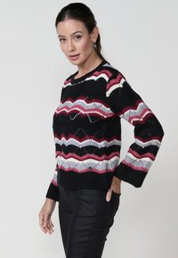 Pull en tricot avec un motif en zigzag noir, rose, gris et blanc. Encolure ronde et manches longues et larges. Fini texturé.