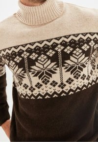 Mörkbrun stickad tröja med en krämfärgad, mönstrad ok som har geometriska mönster och blommotiv. Hög ribbad krage. Mjuk textur.