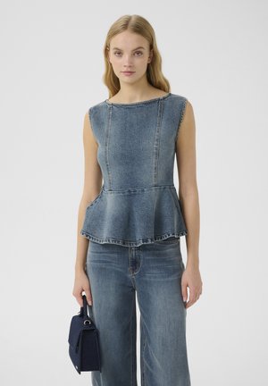 Top in denim a peplum con scollatura a barca, cuciture visibili e orlo svasato. Abbinato a jeans a gamba larga e una piccola borsa blu.