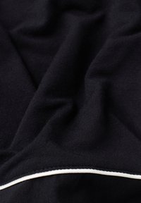 Černá tkanina s měkkou texturou, s bílým lemováním. Materiál je hladký s jemným žebrovaním a jemnými záhyby.