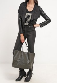 Černá kožená bunda s semišovým límcem, černý top, tmavé džíny, černé kotníkové boty a velká tmavě zelená taška s dvěma držadly.