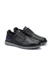 Scarpe in pelle nera con finitura liscia, punta rotonda e suola in gomma grigia a contrasto. Presentano lacci, un colletto imbottito e cuciture sottili.