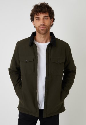 Olive green jacket with black corduroy collar, button front, two chest pockets, and long sleeves; smooth fabric and relaxed fit.