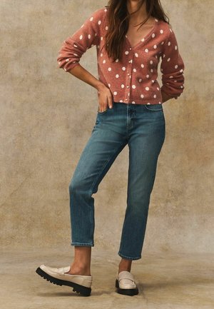 Růžový cardigan s puntíky vyrobený z měkkého materiálu, doplněný modrými džíny a krémovými mokasíny s černou platformou.