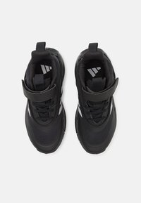 Schwarze Sportschuhe aus Mesh- und Synthetikmaterial, mit einem Klettverschlussriemen, strukturierten Sohlen und weißen Akzenten an den Seiten.