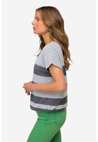 Top corto de rayas grises y blancas con una textura de lunares, combinado con pantalones verdes ajustados. La vista lateral resalta la silueta.
