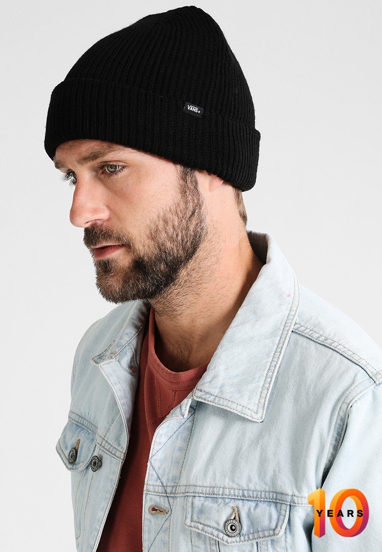 Cappello a beanie a coste nere indossato da un uomo, abbinato a una giacca di jeans azzurro chiaro e una camicia color ruggine. Presenta un piccolo tag con il logo sul beanie.