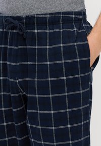 Pantalons de lounge à carreaux bleu marine avec une taille à cordon de serrage, présentant des lignes blanches en grille et des poches latérales, fabriqués en tissu en coton doux.