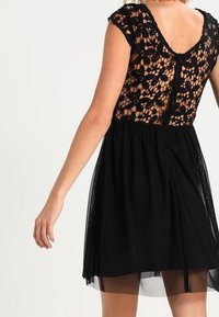 Vestido negro con un corsé de encaje ajustado que presenta patrones florales, un escote en la espalda y una falda de tul fluida.