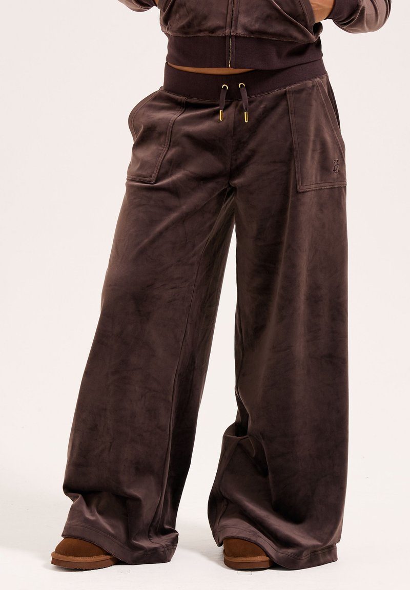 Wide-leg pants in dark brown, made of soft velvet. Features elastic waistband with drawstrings, large front pockets, and subtle logo detail.