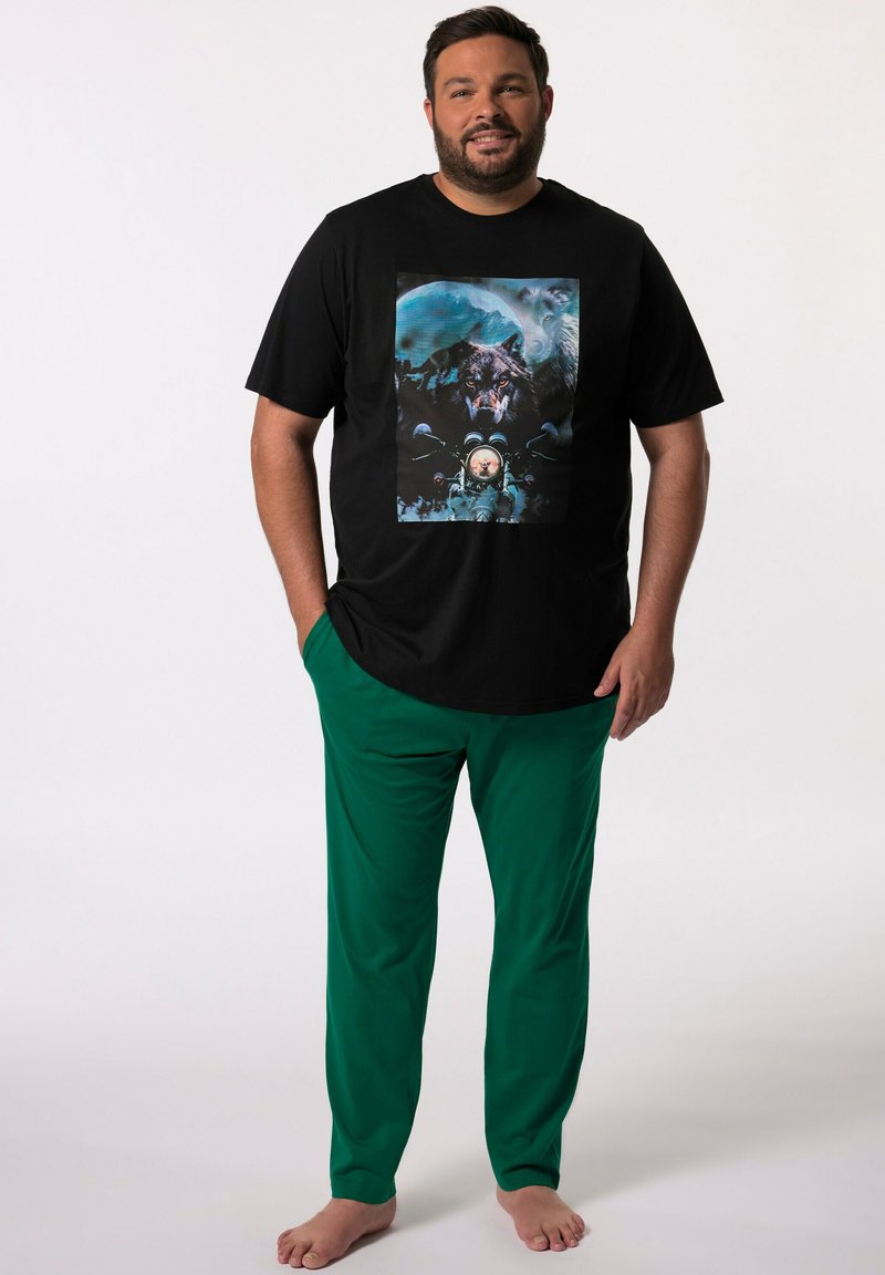 Schwarzes T-Shirt mit einem bunten Grafikdruck, der einen Wolf und einen Astronauten zeigt; kombiniert mit grünen Hosen; beide Kleidungsstücke haben eine lässige Passform und sind weich.