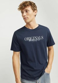 Granatowa bawełniana koszulka z krótkim rękawem, z białym napisem "ORIGINALS Worldwide co. 1990" na piersi oraz okrągłym dekoltem.
