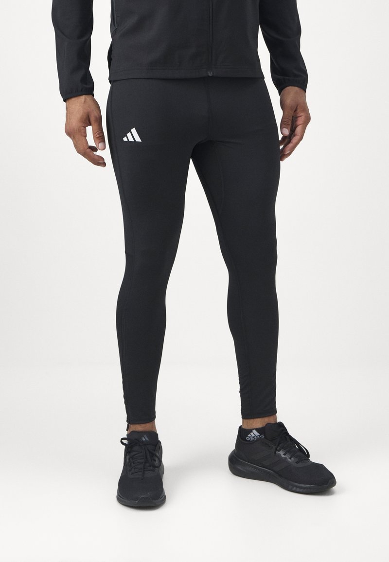 Czarne legginsy sportowe o dopasowanym kroju, z teksturowanej tkaniny, z białym logo Adidas na lewym udzie. W zestawie z czarnymi butami sportowymi.
