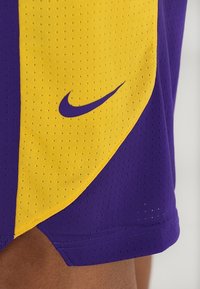 Luonnonvaaleat ja keltaiset Nike urheilushortsit, jotka on valmistettu verkkomateriaalista. Ominaisuuksiin kuuluu perforoitu pinta, swoosh-logo ja kulmajärjestys väripaneelissa.