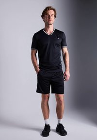 Conjunto atlético preto com uma t-shirt em V com detalhes brancos e calções a condizer. Inclui ténis pretos e meias brancas.