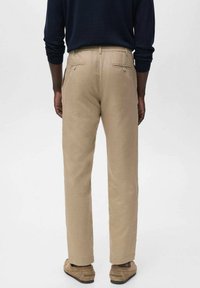 Pantalon beige en coton, avec une coupe droite, deux poches arrière à fermeture bouton et une texture lisse.