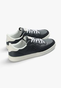 Schwarze Ledersneaker mit einer weißen Gummisohle, die ein Totenkopf-und-Kreuze-Motiv aufweisen, weiße Schnürsenkel und perforierte Details an der Zehe.