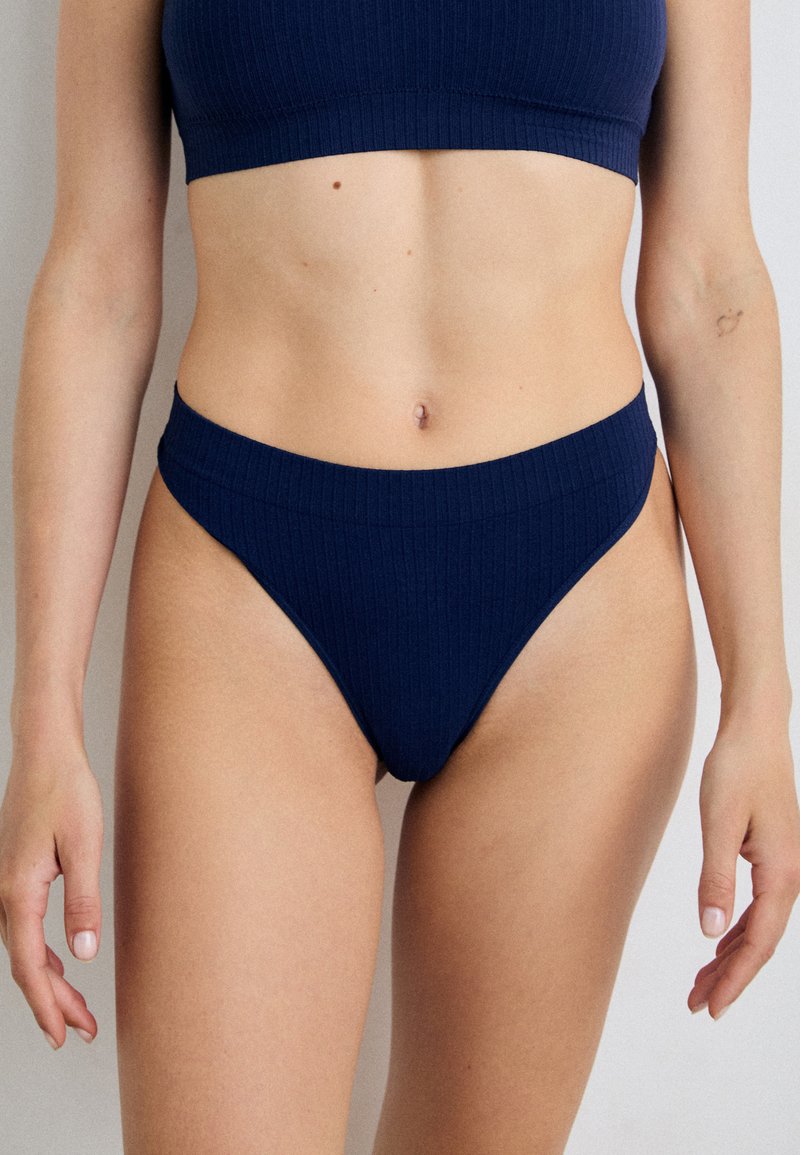 Navy ribbattuinen bikinit, jossa on bralette-yläosa ja korkeavyötäröiset thong-alushousut, joissa on sileä kangas ja saumaton muotoilu.