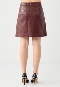 Een bordeauxleren rok met een gladde textuur, voorzien van een rechte snit en een tailleband, aangevuld met zwarte hoge hakken.