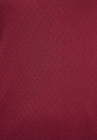 Tejido burdeos con un patrón texturizado de pequeños diamantes, hecho de un material de punto elástico, que presenta una superficie suave y un brillo sutil.