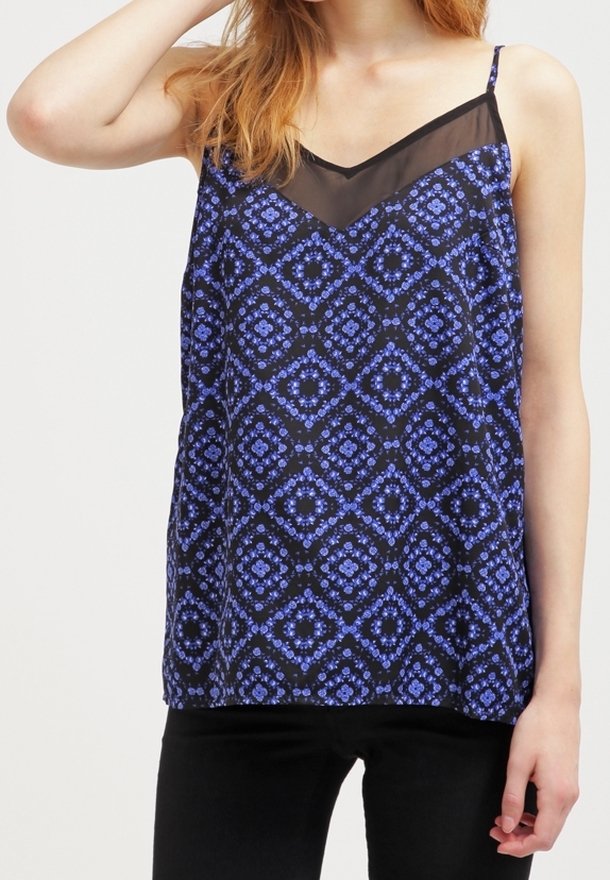 Femme portant un haut noir sans manches avec des motifs floraux géométriques bleus et un panneau en mesh noir transparent au niveau du décolleté.