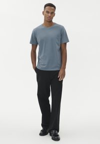 Modré tričko s krátkým rukávem a kulatým výstřihem, kombinované s černými kalhotami rovného střihu a černými botami, na bílém pozadí.