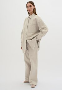 Helles graues, strukturiertes Zweiteiliges Outfit mit einem durchgeknöpften Hemd mit einer Tasche und weiten Hosen, beide mit dezentem Muster.