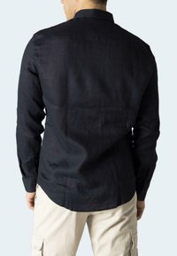 Camicia a maniche lunghe blu scuro in lino con orlo curvo, polsini con bottoni e colletto classico, vista da dietro.