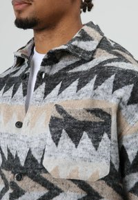 Wollen overhemdjack met een zigzagpatroon in zwart, grijs en beige; knoopsluiting, puntige kraag en een enkele borstzak.