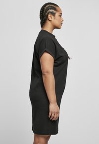 Robe t-shirt en coton noir avec des manches courtes, une coupe décontractée et une longueur au genou. Texture lisse avec un minimum de détails.