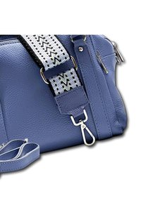 Sac en cuir bleu avec une finition texturée, doté d'une bandoulière amovible avec un motif en zigzag noir et blanc, détails en matériel argenté.