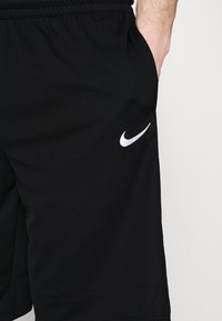 Pantalones cortos deportivos negros hechos de tejido texturizado, con una cinturilla elástica y bolsillos laterales. Un pequeño logo blanco de Nike se encuentra en el lado izquierdo.
