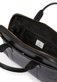 Svart läderväska med dragkedjestängning, med en innerficka och svart strukturerad foder. Guldiga detaljer synliga.