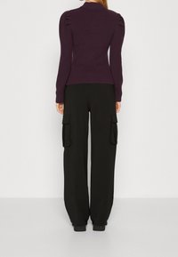 Žebrovaný tmavě fialový svetr s nápadnými nadýchan�ými rameny, kombinovaný s volnými černými cargo kalhotami s předními kapsami.