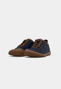 Chaussures bleu marine avec lacets marron, tige en daim et semelle en caoutchouc. Bout arrondi, couture minimale et logo Camper sur la languette.