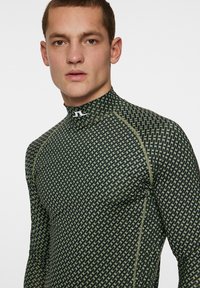 Mörkgrön långärmad atletisk topp med geometriskt mönster och hög krage. Har en åtsittande passform och kontrasterande sömdetaljer.