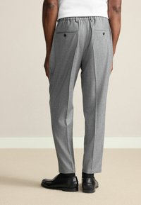 Gray tailored trousers with a textured finish, elastic waistband, two back pockets with buttons, and a straight-leg design. Black shoes are worn.
