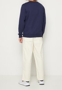 Marineblauwe sweatshirt met geribde manchetten, witte wijde broek en witte sneakers. Eenvoudig ontwerp met een relaxte pasvorm.