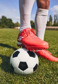 Ghete de fotbal albastre strălucitoare cu suprafață texturată și accente albe, așezate pe o minge de fotbal alb-negru, pe iarbă verde.
