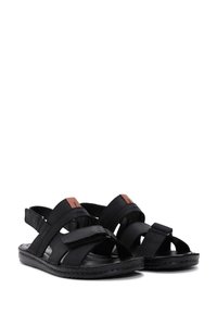Sandalias negras con múltiples correas entrelazadas de tela, que cuentan con cierres ajustables de Velcro y acentos marrones en la parte superior.