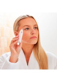 Apparaat: een witte en roze gezichtsbehandeling tool met een puntige tip, vastgehouden door een persoon in een witte kamerjas, met een glad, gestroomlijnd ontwerp en metalen accenten.